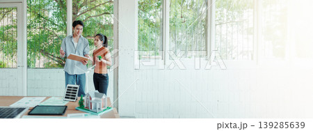 Architects reviewing building model and plans in bright studio with solar panel concept and greenery outside windows. Architects reviewing building model and plans in bright studio with solar panel concept and greenery outside windows. 139285639
