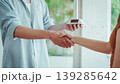 Close-up of two people shaking hands while one holds a smartphone with blank screen, suggesting mobile payment confirmation or business agreement in a bright indoor setting. 139285642