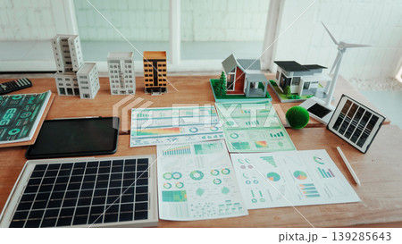Desk workspace with solar panel, wind turbine model, smart home miniatures and printed energy analytics charts, illustrating renewable energy planning and sustainable city development. Desk workspace with solar panel, wind turbine model, smart home miniatures and printed energy analytics charts, illustrating renewable energy planning and sustainable city development. 139285643