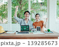 Smiling young team celebrates sustainable energy project at desk with laptop showing ESG dashboard, wind turbines and solar panel models in bright office with green view. 139285673