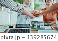 Team stacking hands over desk with solar panel, wind turbine model and eco house mockup in modern office, symbolizing collaboration on renewable energy and sustainable construction. 139285674