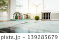 Miniature eco home models with solar panel and wind turbine on a desk, suggesting sustainable architecture, renewable energy planning, and green building design. 139285679