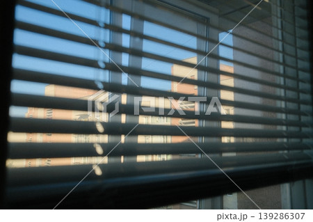 View through blinds shows exterior of building and blue sky, sunny day 139286307