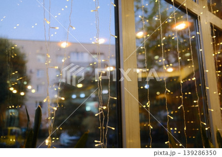 String lights hang by a window. A building can be seen through the glass 139286350