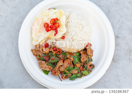 Thai basil beef stir fry with rice and fried egg topped with chili spicy savory street food meal popular Thai cuisine fresh herbs and rich flavor 139286367