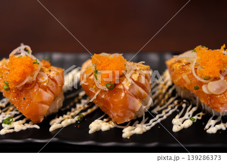 Close up salmon sushi bites topped with roe and sauce on black plate fresh seafood Japanese cuisine gourmet presentation rich flavor and texture ready to eat 139286373