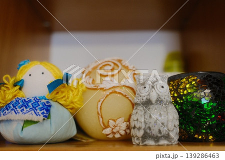 A small doll, decorated egg, owl figure, and candle holder sit on a wooden shelf 139286463