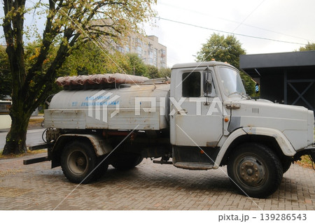 A weathered water tank truck, marked Lutskvodokanal, stands on a brick paved city street 139286543