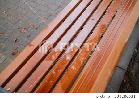 Raindrops cover an empty wooden bench in a park. Fallen leaves are scattered nearby Raindrops cover an empty wooden bench in a park. Fallen leaves are scattered nearby 139286631
