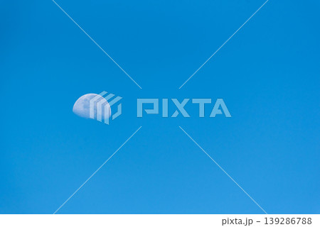 Half moon visible in bright blue sky during daytime minimal composition with large copy space calm atmosphere and natural light ideal for background or space concept Half moon visible in bright blue sky during daytime minimal composition with large copy space calm atmosphere and natural light ideal for background or space concept 139286788