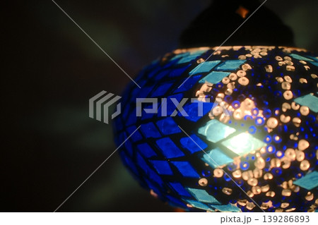 Light shines through a blue, mosaic-tiled turkish lamp, creating a warm glow Light shines through a blue, mosaic-tiled turkish lamp, creating a warm glow 139286893