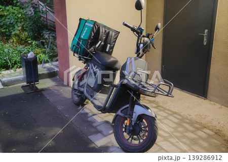 A food delivery moped with a bag sits parked on a paved street A food delivery moped with a bag sits parked on a paved street 139286912