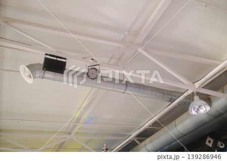 A low angle shows ducts, lamps, lighting, and a white ceiling with beams A low angle shows ducts, lamps, lighting, and a white ceiling with beams 139286946
