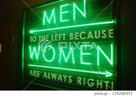A bright green neon sign displays gender-specific bathroom instructions with a joke A bright green neon sign displays gender-specific bathroom instructions with a joke 139286951