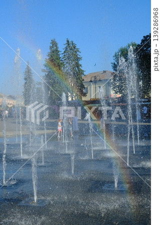 A child plays in a water fountain. Rainbows appear in the fountain sprays in the summer A child plays in a water fountain. Rainbows appear in the fountain sprays in the summer 139286968