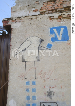 A bird and letter V are painted onto the side of an old, crumbling brick building A bird and letter V are painted onto the side of an old, crumbling brick building 139287092