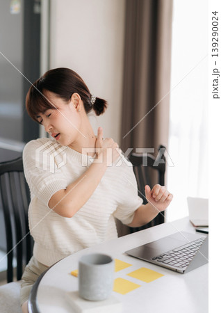 Tired young asian woman with neck pain feeling stress and exhausted during remote business project work using laptop computer and smartphone app at modern home desk 139290024