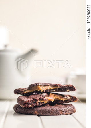 Stack Of Chocolate Caramel Cookies Close-Up On White Table With Coffee Cup In Background 139290651