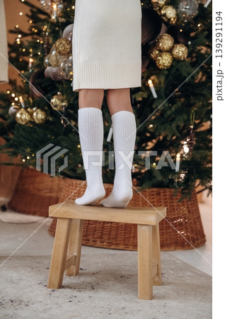 Particle view of girl's legs that is standing on a stool and decorates the Christmas tree 139291194