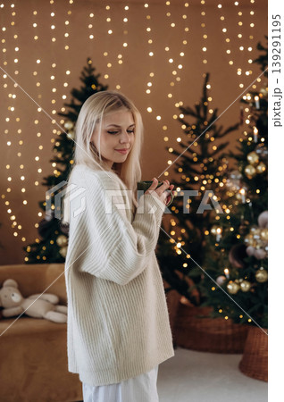 Beautiful woman is standing in the room with New Year garlands and fir 139291195