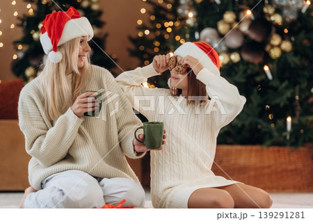 Fun with cookies, sitting on the floor. Mother and daughter are celebrating New Year at home in domestic room Fun with cookies, sitting on the floor. Mother and daughter are celebrating New Year at home in domestic room 139291281