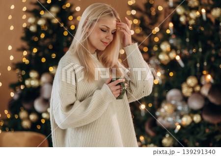 Standing and posing. Beautiful woman is standing in the room with New Year garlands and fir 139291340