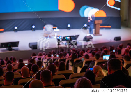 Conference audience watching speaker on stage during professional event with cameras Conference audience watching speaker on stage during professional event with cameras 139291371