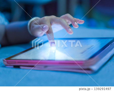 Close-up of a cute little Asian girl using a digital tablet at home, focused child playing games or learning online, soft indoor lighting. Close-up of a cute little Asian girl using a digital tablet at home, focused child playing games or learning online, soft indoor lighting. 139291497