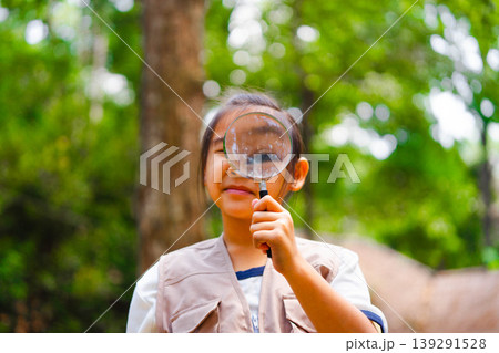 Curious young Asian girl using a magnifying glass to explore tree bark in a pine forest, nature education and outdoor science learning concept. Curious young Asian girl using a magnifying glass to explore tree bark in a pine forest, nature education and outdoor science learning concept. 139291528