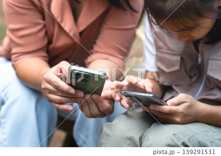 Asian mother and daughter using smartphone for digital learning and research in a park, family technology and education concept. 139291531