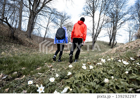 Two hikers walking on a trail through a forest, surrounded by wildflowers. Two hikers walking on a trail through a forest, surrounded by wildflowers. 139292297