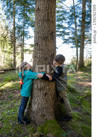 Brother and sister embrace a large tree in a forest, enjoying nature's beauty. Brother and sister embrace a large tree in a forest, enjoying nature's beauty. 139292309