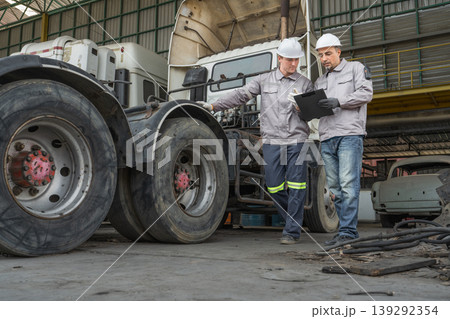 Caucasian and Middle Eastern mid-adult male technicians walk through an Asian container yard while holding a clipboard 139292354
