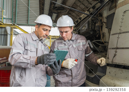 Caucasian and Middle Eastern mid-adult male mechanics examining a truck engine in an industrial maintenance garage in Thailand, Asia, for ensuring heavy transport vehicle reliability 139292358
