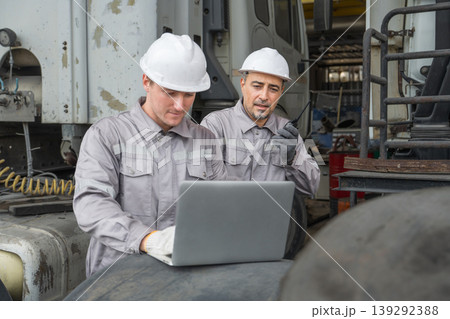 Caucasian and Middle Eastern mid-adult male mechanics repairing truck engine with laptop in Asian yard 139292388