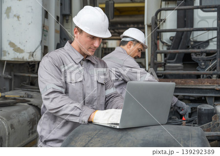 Caucasian and Middle Eastern mid-adult male mechanics repairing truck engine with laptop in Asian yard Caucasian and Middle Eastern mid-adult male mechanics repairing truck engine with laptop in Asian yard 139292389