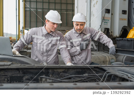 Caucasian and Middle Eastern mid-adult male mechanics repairing truck engine with laptop in Asian yard 139292392