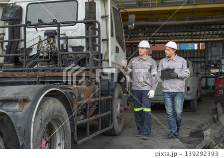 Caucasian and Middle Eastern mid-adult male technicians walk through an Asian container yard while holding a clipboard 139292393