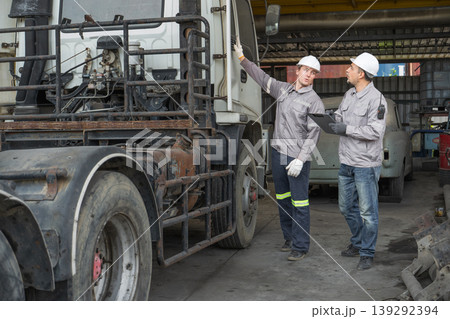 Caucasian and Middle Eastern mid-adult male technicians walk through an Asian container yard while holding a clipboard 139292394