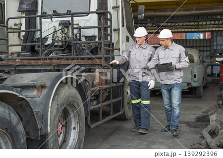 Caucasian and Middle Eastern mid-adult male technicians walk through an Asian container yard while holding a clipboard 139292396