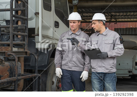 Caucasian and Middle Eastern mid-adult male technicians walk through an Asian container yard while holding a clipboard 139292398