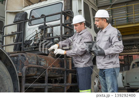 Caucasian and Middle Eastern mid-adult male technicians walk through an Asian container yard while holding a clipboard 139292400