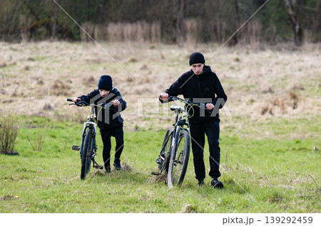 Two boys walk their bikes across a grassy field, enjoying an outdoor adventure. Two boys walk their bikes across a grassy field, enjoying an outdoor adventure. 139292459
