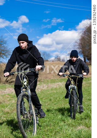 Two young cyclists enjoying a sunny day outdoors, riding their bikes across a grassy field. 139292460