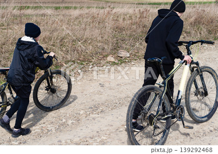 Two kids walking their bikes down a dirt road. A sunny day outdoors. Two kids walking their bikes down a dirt road. A sunny day outdoors. 139292468