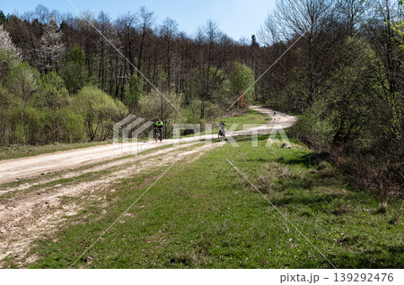 Cyclists on a dirt road through a forest. Sunny day, lush green landscape. Cyclists on a dirt road through a forest. Sunny day, lush green landscape. 139292476