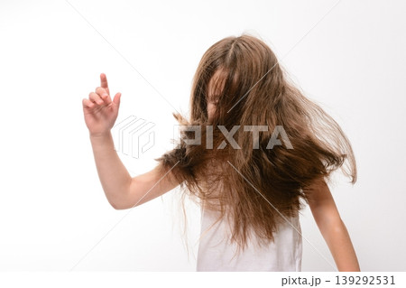 Girl with long brown hair playfully tosses her head, hand raised in a gesture. Girl with long brown hair playfully tosses her head, hand raised in a gesture. 139292531