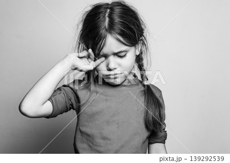 A young girl wipes away a tear, her sadness evident in her expression. 139292539
