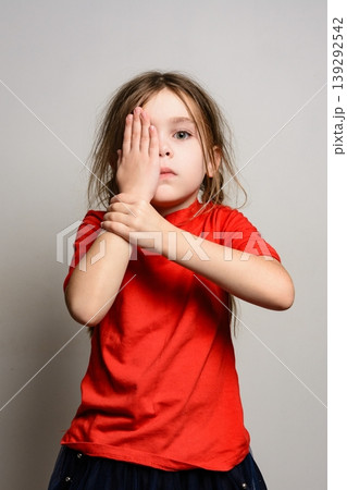 Young girl covering one eye with her hand, playful expression. Young girl covering one eye with her hand, playful expression. 139292542