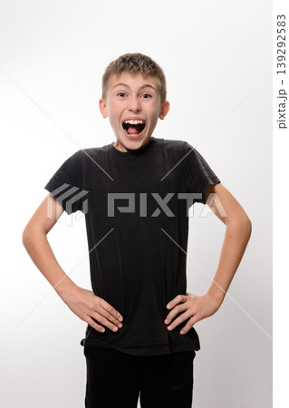 A young man stands against a plain white background with his hands on his waist. He has a sarcastic smile on his face. A young man stands against a plain white background with his hands on his waist. He has a sarcastic smile on his face. 139292583